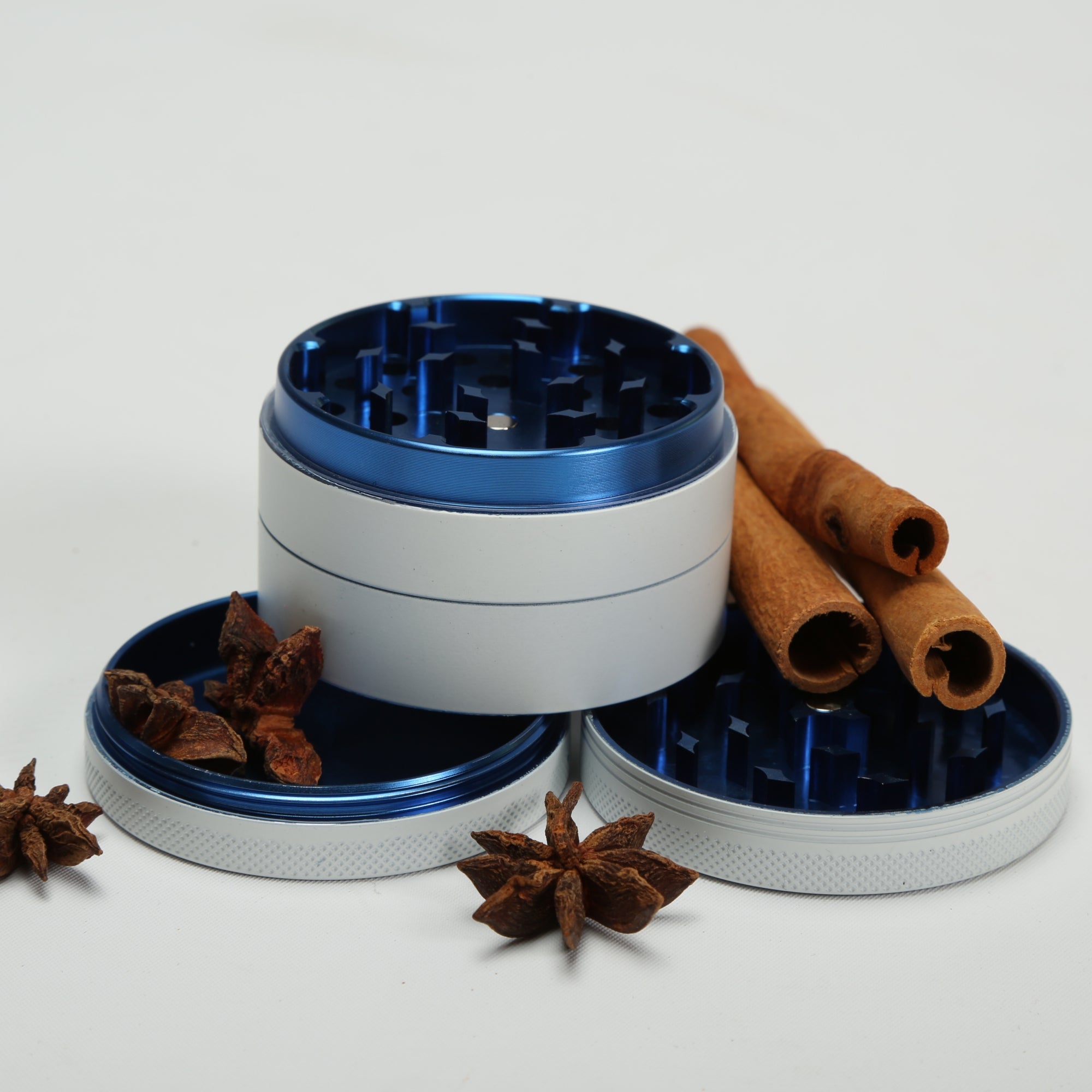 Metal grinder with blue accents on a white background with cinnamon sticks and star anise.