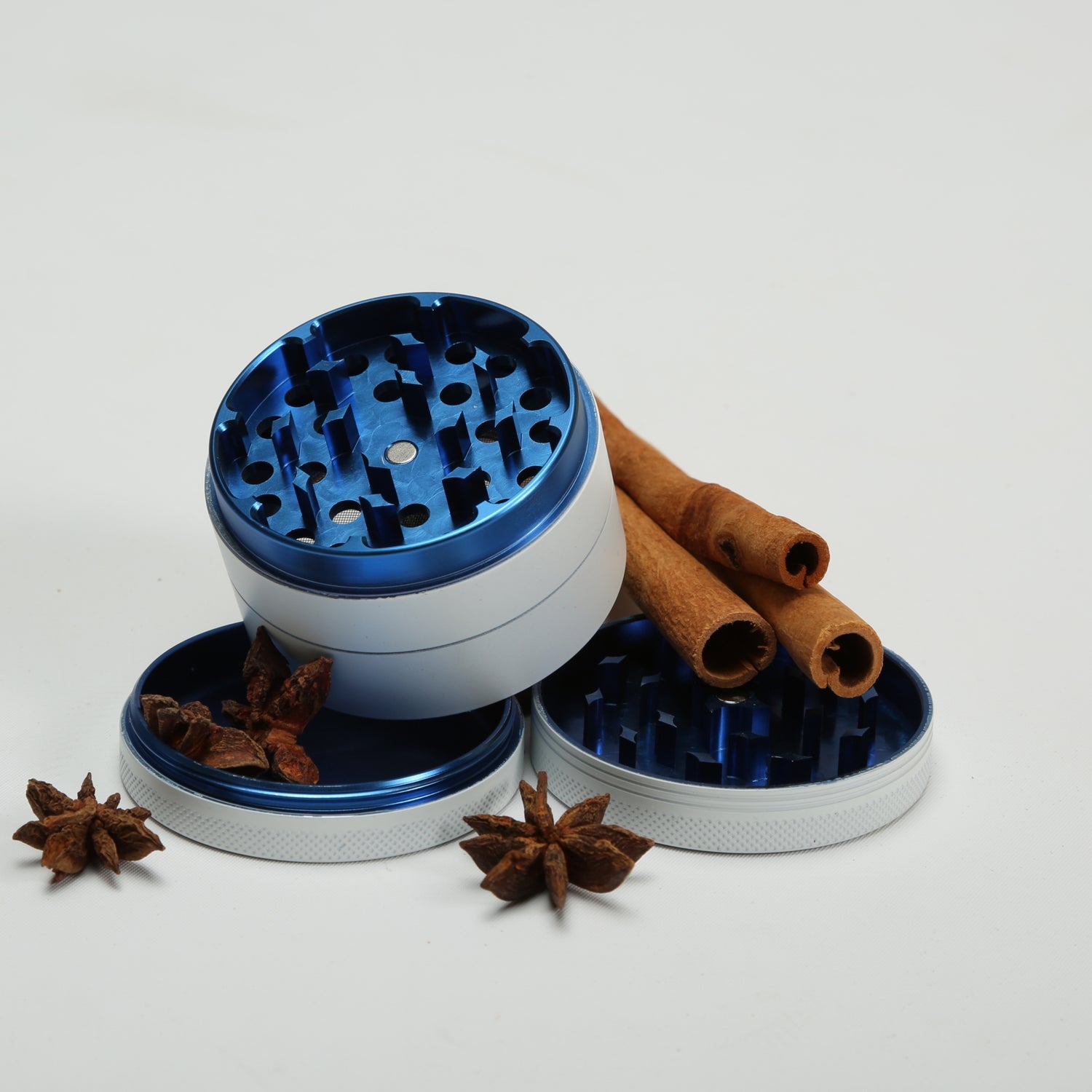 Blue and silver metal grinder with cinnamon sticks and star anise on a white background 
