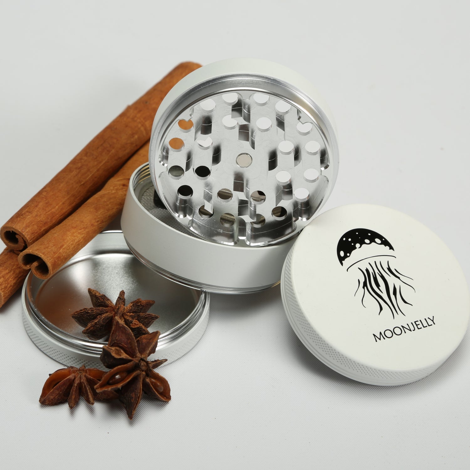 White herb grinder with star anise and cinnamon sticks on a light gray background 