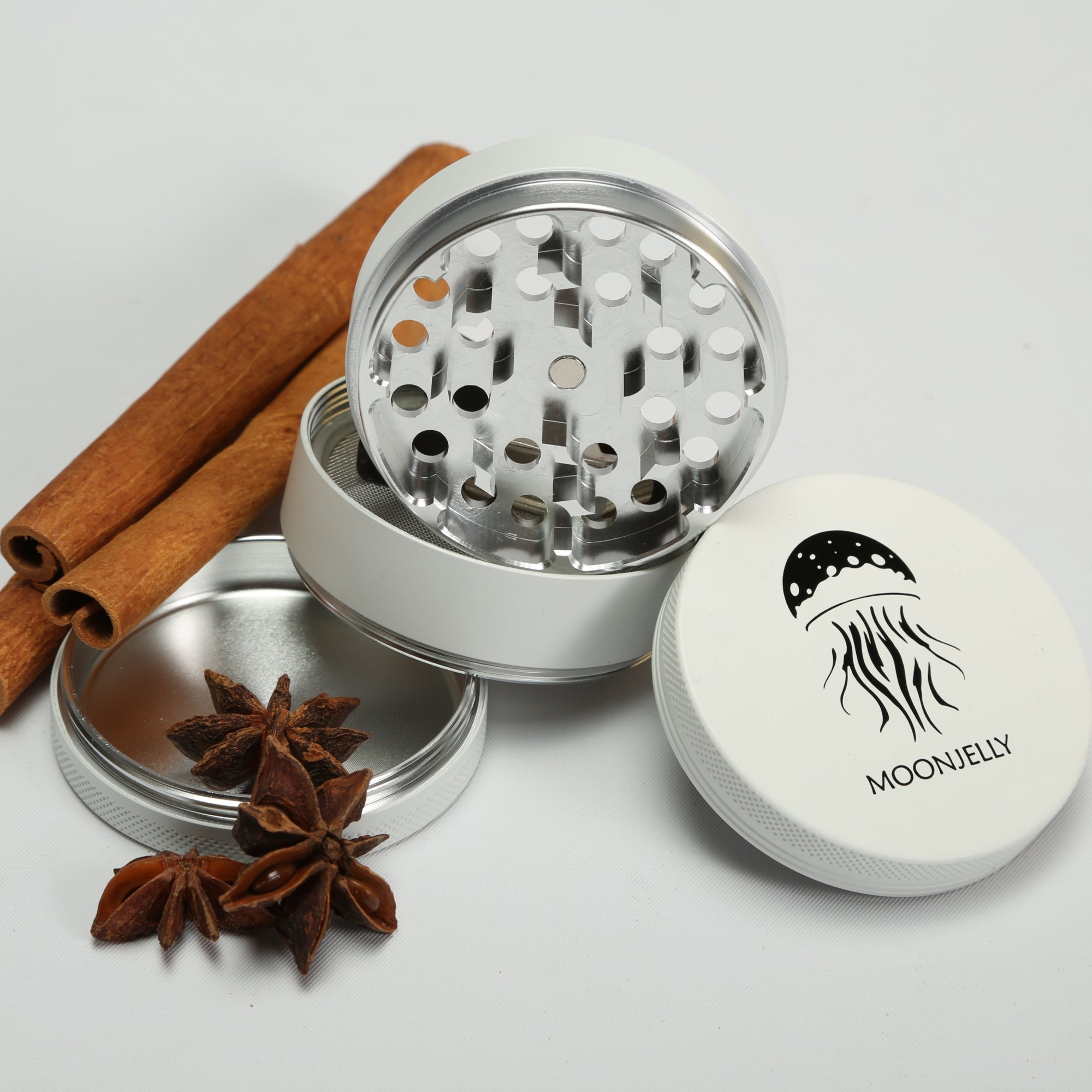 White herb grinder with star anise and cinnamon sticks on a light gray background 